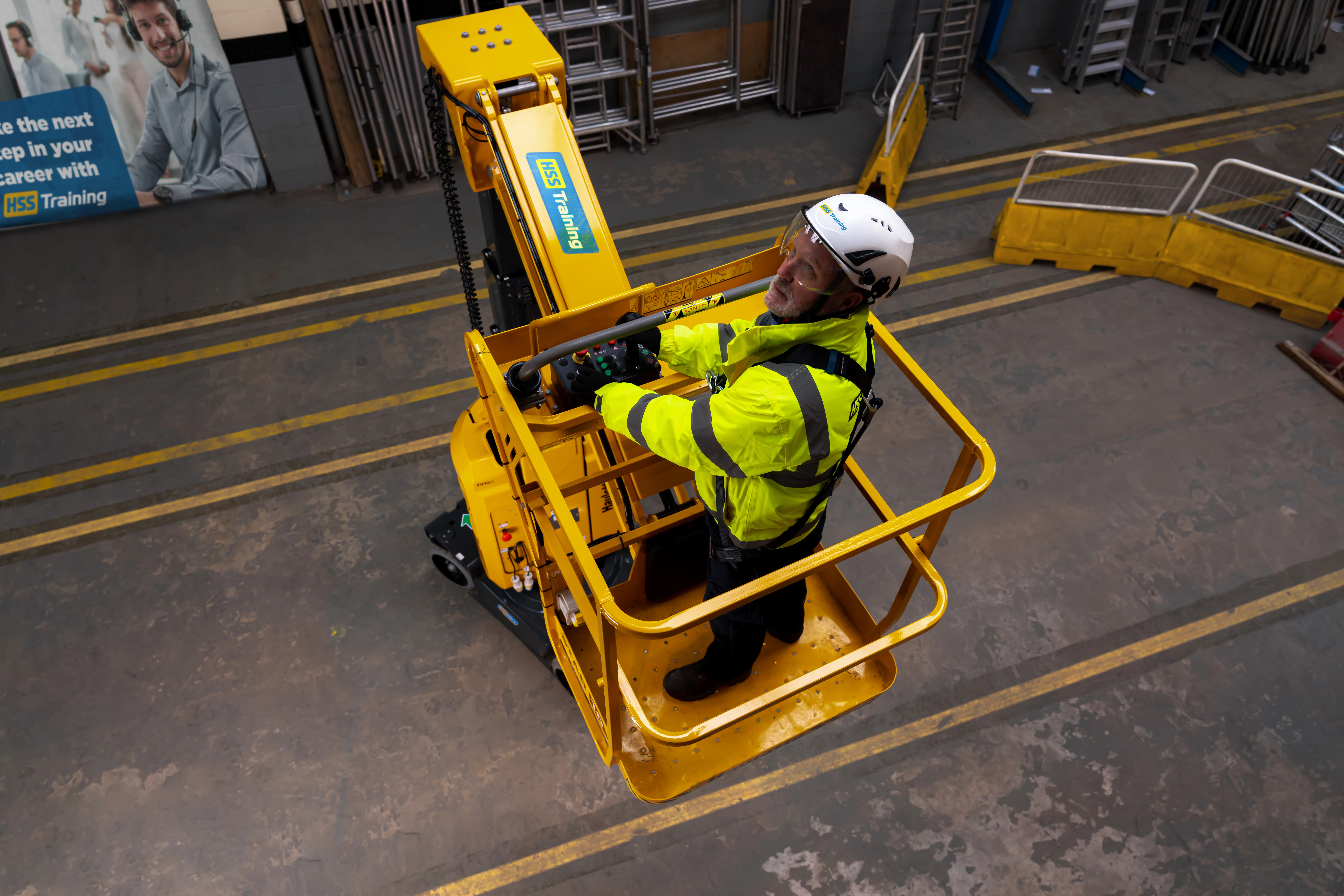 Man in hi-vis jacket wearing a harness and a helmet operating Work at Height machinery on a HSS Training course